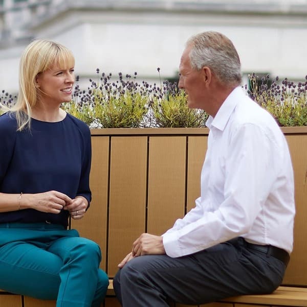 A man and woman sat talking in an outdoors courtyard in front of a plant